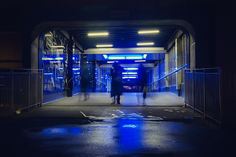 Blurred figures walking through a blue-lit urban tunnel at night