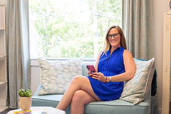 Smiling woman in blue dress using smartphone on sofa
