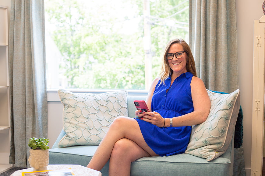 Smiling woman in blue dress using smartphone on sofa