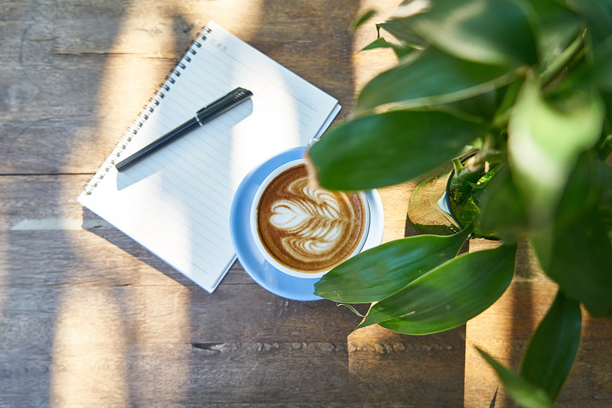 Flat lay of latte art coffee, notebook, and plant on wooden table