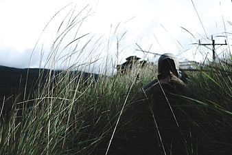 Person in Hoodie Sitting in Tall Grass Field