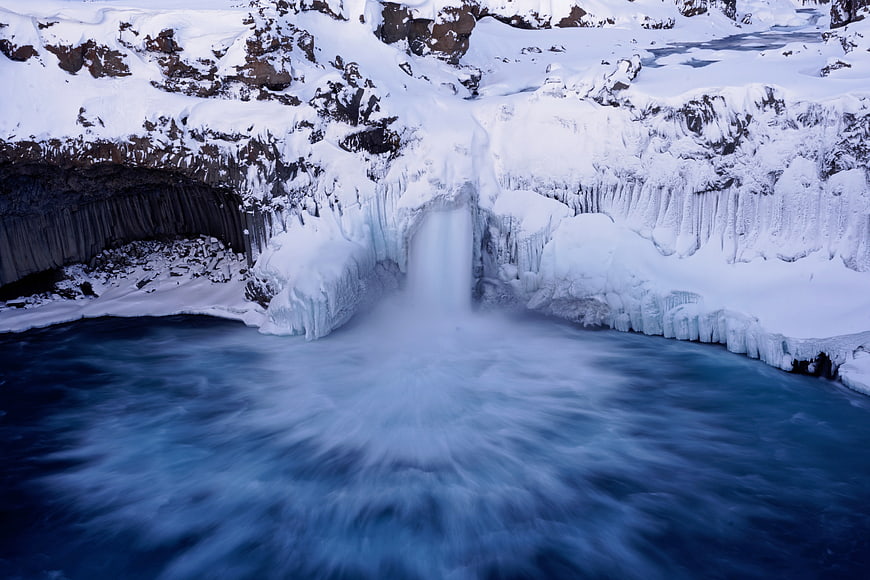 Frozen waterfall cascading into icy blue river in winter landscape