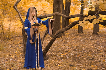 Young woman in medieval blue robe reading book in autumn forest
