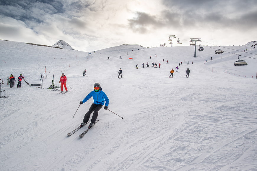 Skier in Blue Jacket Descending Snowy Mountain Slope