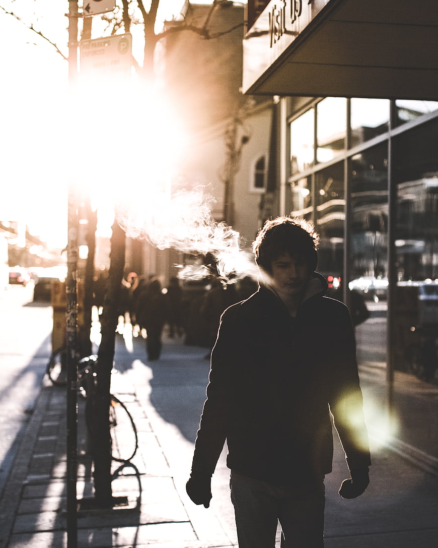 Man exhaling smoke on sunlit city street