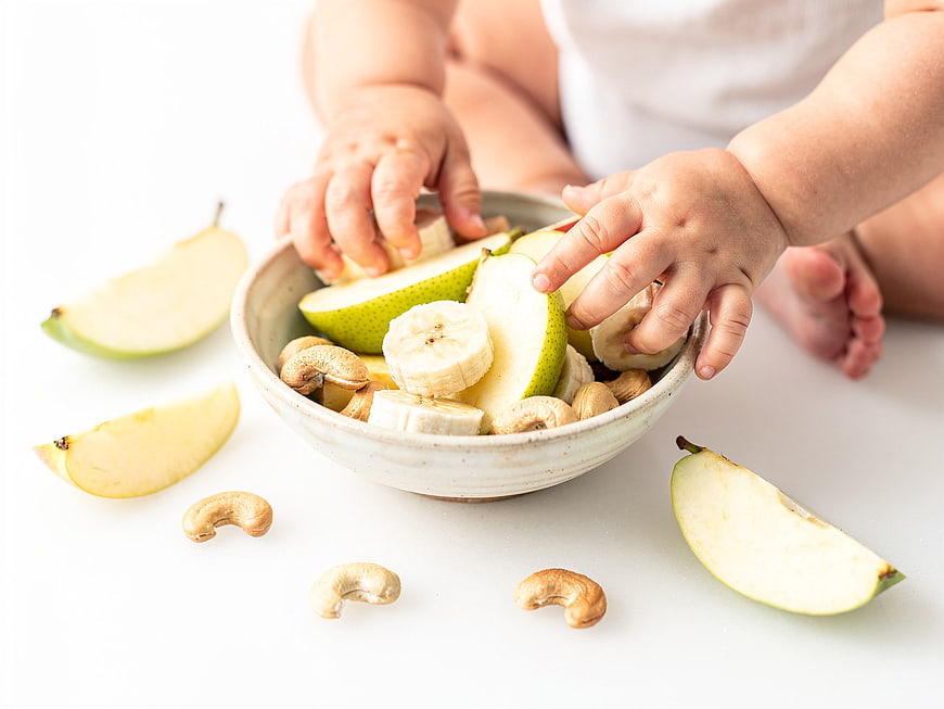 Toddler Hands Reaching for Healthy Fruit and Nut Snack Bowl