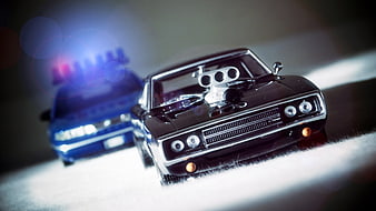 Black Dodge Charger Model Car With Blue Police Car Background