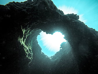 Heart-shaped underwater cave opening with sun rays