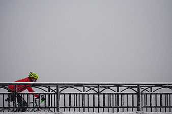 Cyclist in red jacket riding bicycle on snowy bridge
