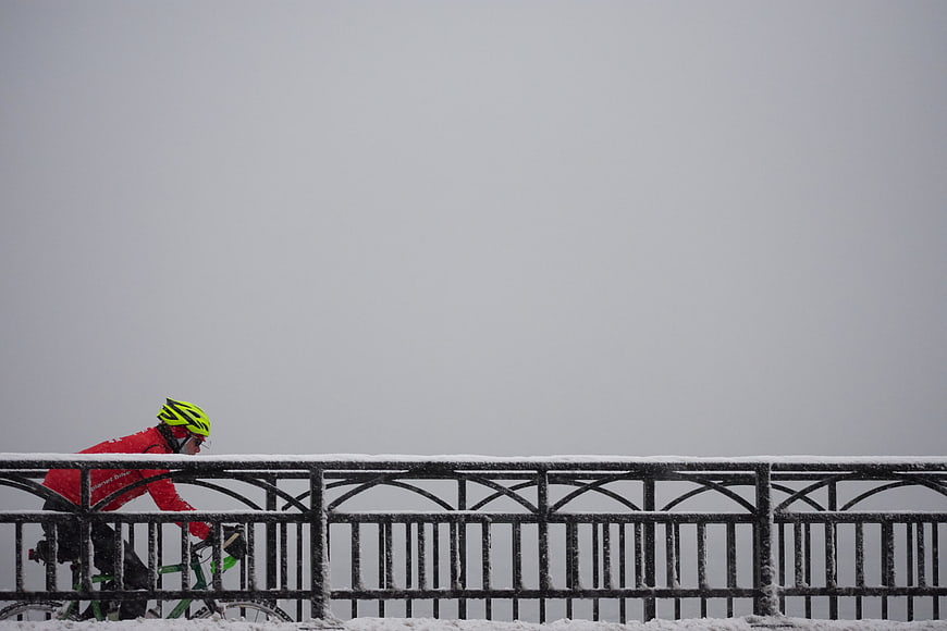 Cyclist in red jacket riding bicycle on snowy bridge