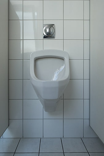 White Ceramic Urinal Mounted On White Tiled Wall