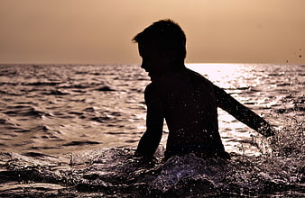Silhouette of Boy Splashing in Ocean at Sunset