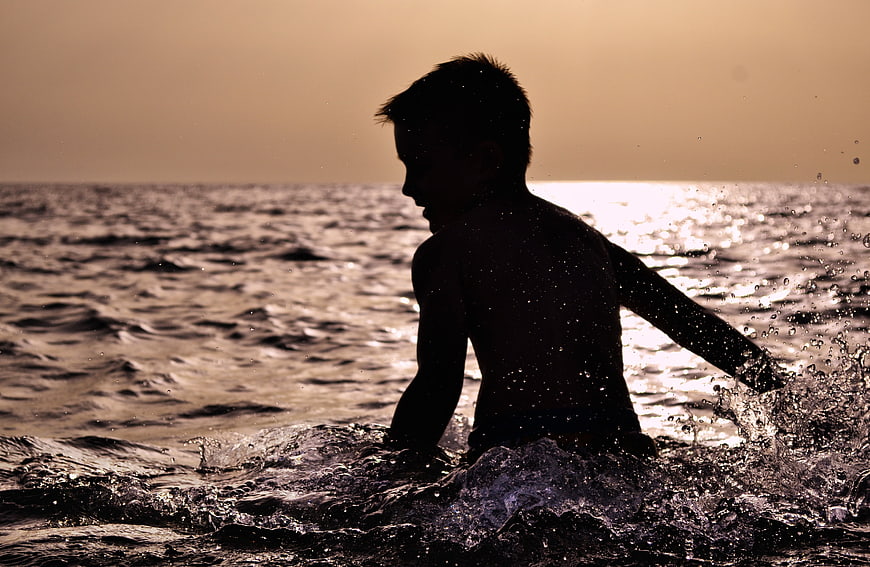 Silhouette of Boy Splashing in Ocean at Sunset