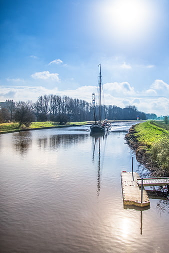 Sailboat navigating a sunny canal with wooden dock