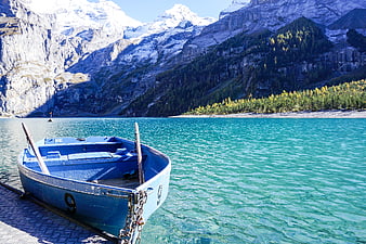 Blue rowboat docked at turquoise alpine lake with snowy mountains