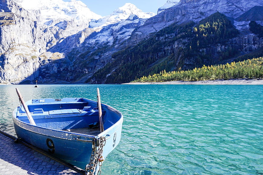 Blue rowboat docked at turquoise alpine lake with snowy mountains