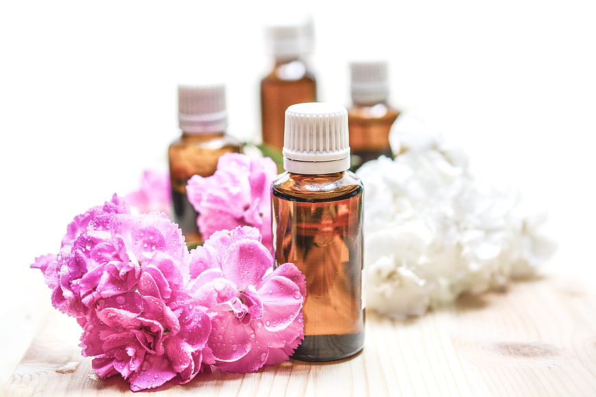 Essential oil bottles with pink and white flowers on wood