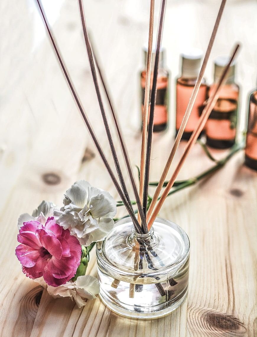 Glass reed diffuser with pink and white flowers on wooden table