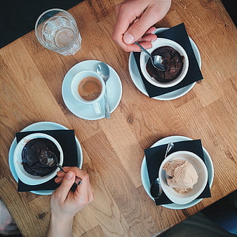 Top view of hands eating chocolate and vanilla ice cream with coffee on wooden table