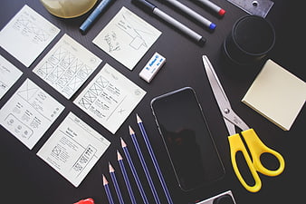 Flat lay of design tools, wireframes, and smartphone on dark desk