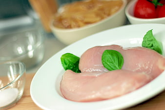 Raw chicken breasts with basil on white plate