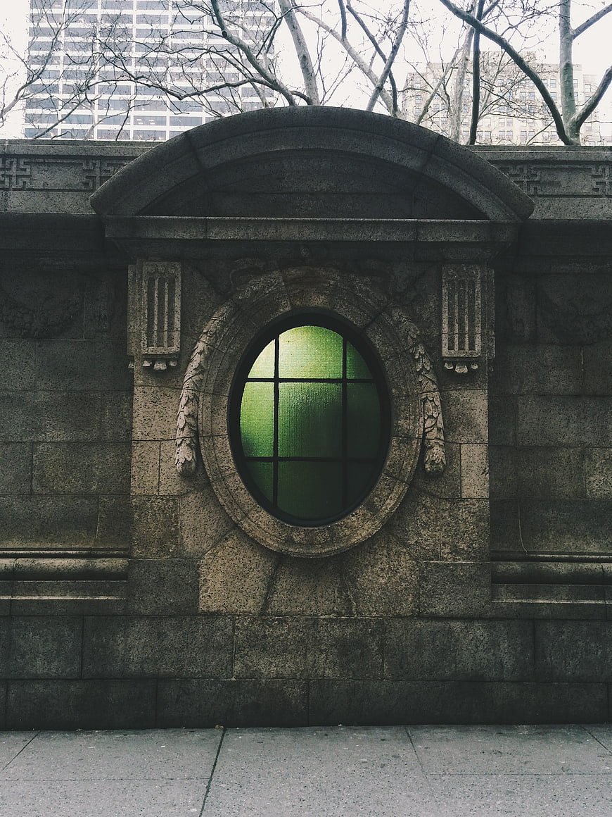 Vintage stone wall with green oval window and city background