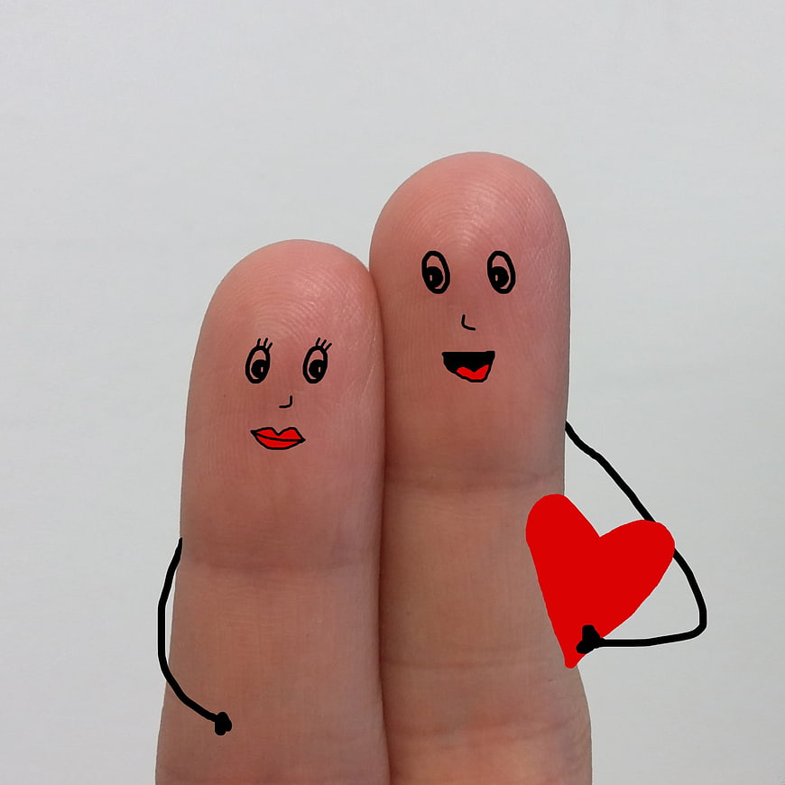 Finger puppets couple holding red heart on white background