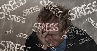 Stressed Man Holding Head Against Chalkboard With Stress Words