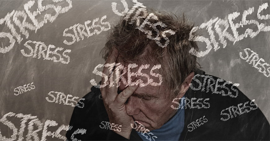 Stressed Man Holding Head Against Chalkboard With Stress Words