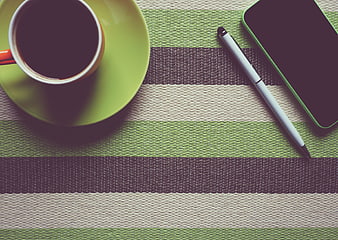 Flat lay of coffee cup, smartphone, and pen on striped placemat