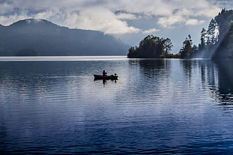 Fisherman in small boat on calm lake with mountain reflections