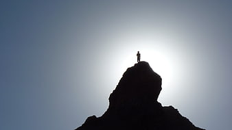 Silhouette of a hiker standing on a mountain peak against a bright sky