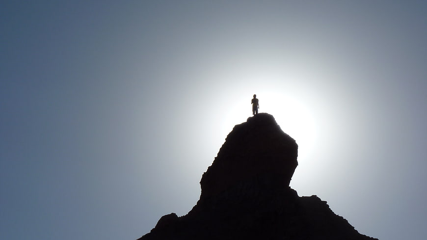 Silhouette of a hiker standing on a mountain peak against a bright sky