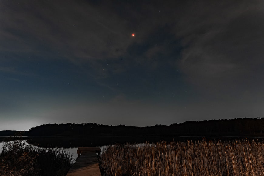 Total Lunar Eclipse Over Lake With Wooden Dock