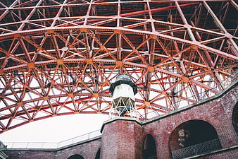 Low angle view of red steel truss bridge over brick lighthouse