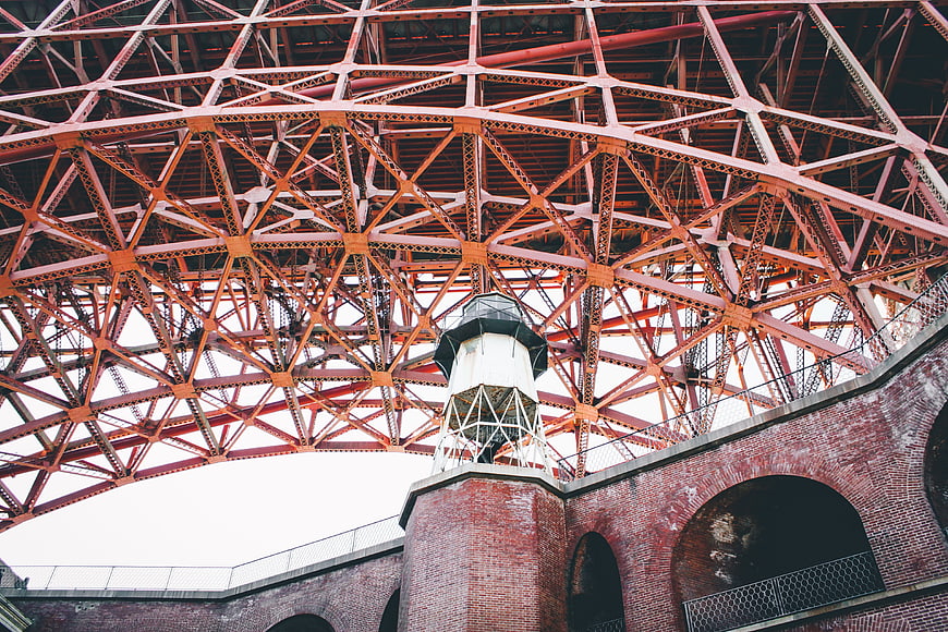 Low angle view of red steel truss bridge over brick lighthouse