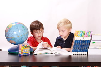 Two young boys studying together with books and a globe