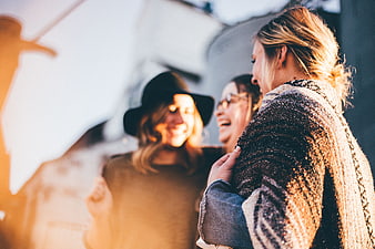 Three happy women laughing together outdoors in golden sunlight