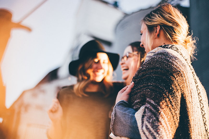 Three happy women laughing together outdoors in golden sunlight