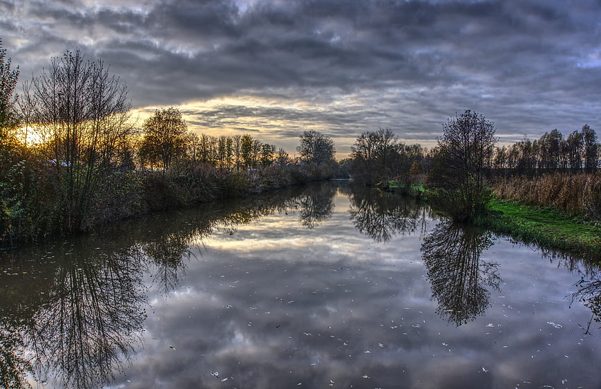 Dramatic sunset reflection on calm river with autumn trees