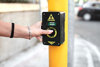 Hand pressing pedestrian crossing button on yellow pole