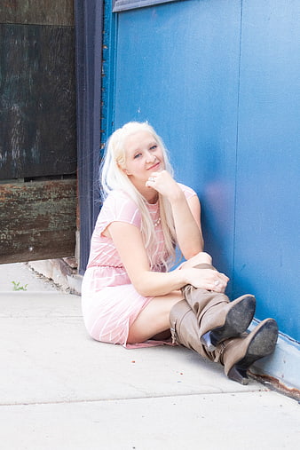 Blonde woman in pink dress sitting against blue wall