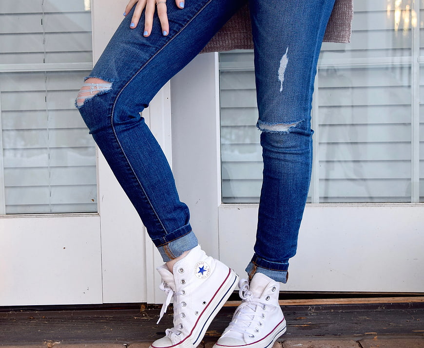 Woman wearing ripped blue jeans and white high-top sneakers