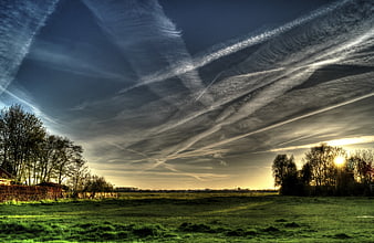 Dramatic Sky with Contrails Over Green Meadow at Sunset