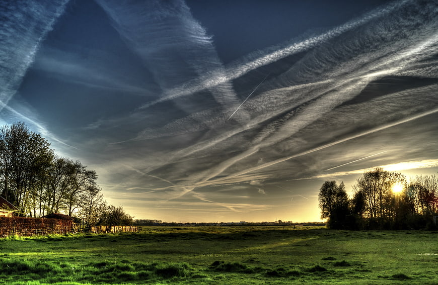 Dramatic Sky with Contrails Over Green Meadow at Sunset