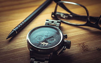 Silver wristwatch, pen, and glasses on wooden desk