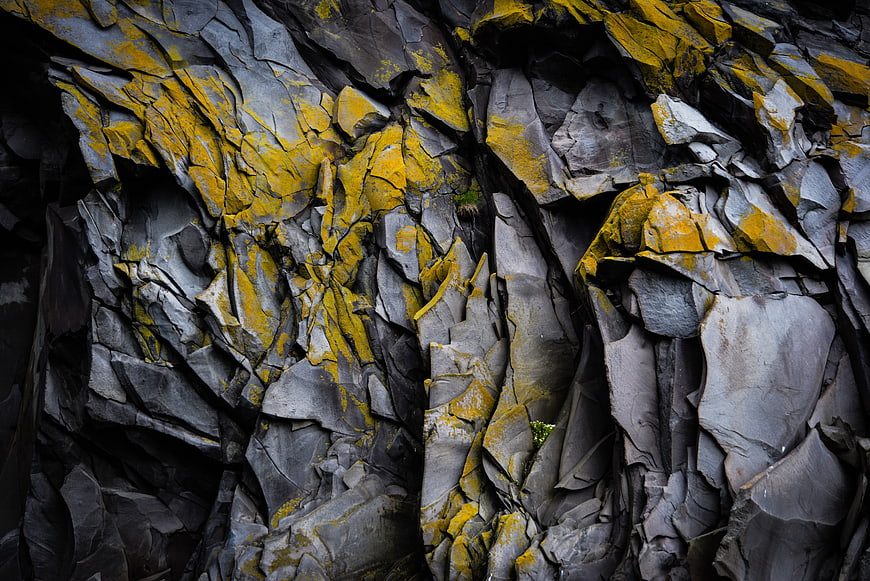 Close-up of jagged gray rock face with yellow lichen patterns