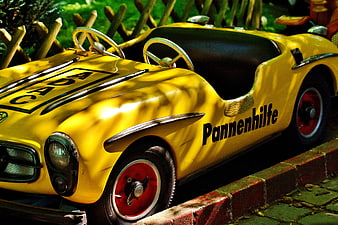 Yellow vintage toy car with Pannenhilfe text parked on brick curb
