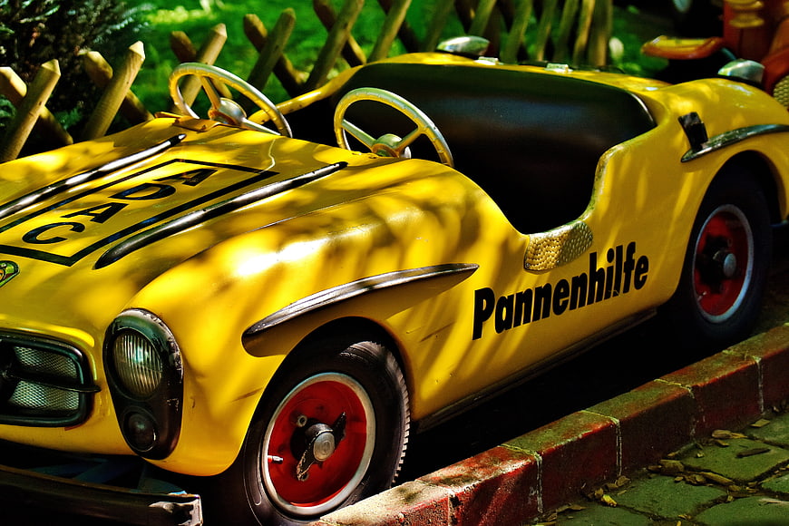 Yellow vintage toy car with Pannenhilfe text parked on brick curb