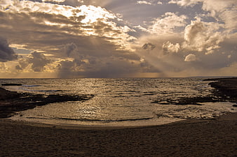 Dramatic sunset over rocky beach with golden sun rays